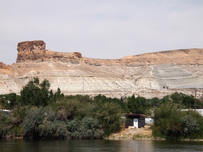 [Grey and sandstone colored rock rising way above the greenery at the riverbank in the foreground. One piece of rock resembles a large (wide) chimney. Within part of the rock on the right side of the image are two dark half circles which are the tunnels for the east and west bound traffic on Interstate 80.]